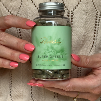 Product photography of Super Greens supplement from Protein.dk in an aesthetic wellness setting.